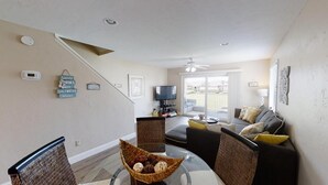 Una sala de estar moderna con una mesa de comedor de vidrio, sillas de mimbre, un sofá y un televisor.