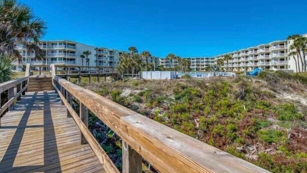 Un paseo marítimo de madera que conduce a un hotel frente al mar, con varios balcones y una vista despejada del océano.