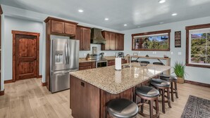 Una cocina moderna con armarios de madera, un refrigerador de acero inoxidable, encimeras de granito y una isla grande con taburetes de bar.