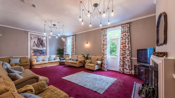 A spacious living room with multiple sofas and armchairs, a large rug, and a television.