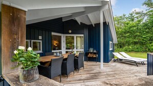 Un área de comedor al aire libre con una mesa y sillas de madera, una planta en maceta y vista de la casa.