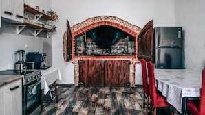 Une cuisine équipée d’un four en pierre, d’un réfrigérateur et d’une table à manger avec des chaises rouges.