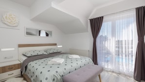 Une chambre à coucher avec un lit, un banc, un miroir et une fenêtre avec des rideaux.