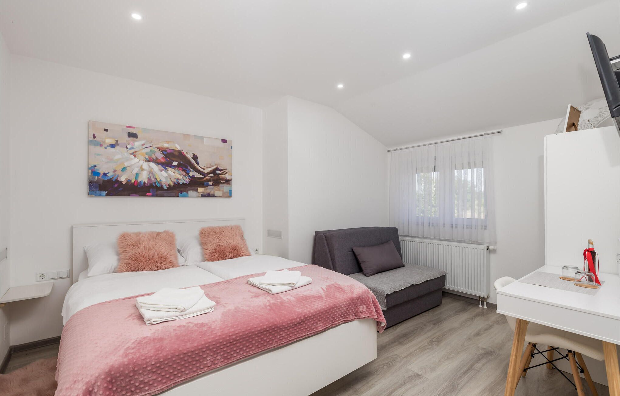 Une chambre à coucher moderne avec un grand lit, un canapé gris, un bureau et un tableau au mur.