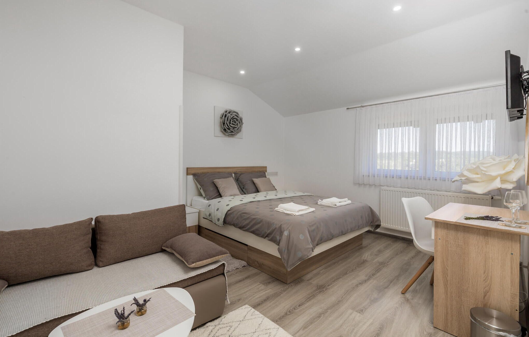 A modern bedroom with a bed, a sofa, a desk, and a radiator.
