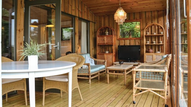 Interno di una baita in legno con mobili in vimini, un televisore ed scaffali con oggetti decorativi.