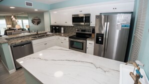 A modern kitchen with white cabinets, stainless steel appliances, and a marble countertop. - D406 Corner Unit, Great View of Pool and Direct Gulf View (Panama City Beach)