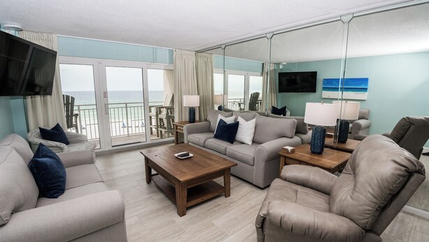 A spacious living room with a large window overlooking the ocean, a flat-screen TV mounted on the wall, and a comfortable seating area with a sofa and armchairs. - D406 Corner Unit, Great View of Pool and Direct Gulf View (Panama City Beach)