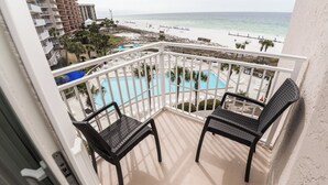 A balcony with two black chairs, a pool, and a beach view. - D406 Corner Unit, Great View of Pool and Direct Gulf View (Panama City Beach)