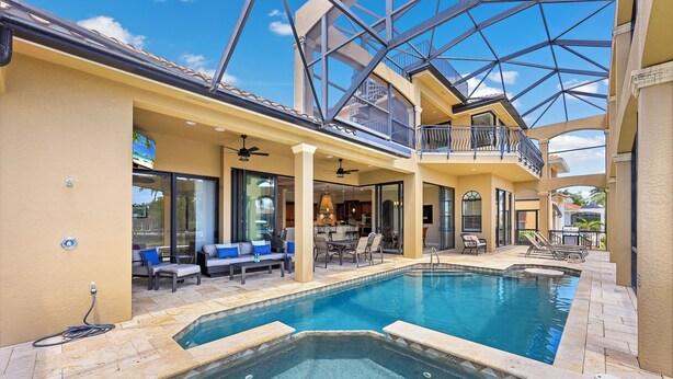 A pool area with a hot tub, lounge chairs, and a covered patio.