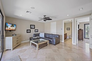 Ein geräumiges Wohnzimmer mit einer Ledersofa, einem Glastisch und einem Deckenventilator.