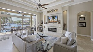 A spacious living room with a large TV, comfortable seating, a fireplace, and a view of a pool.