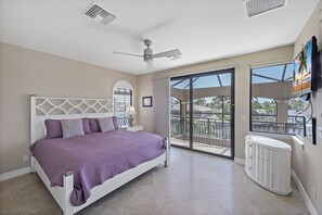 A bedroom with a bed, a ceiling fan, a large window, and a TV. - Opulent Waterfront Home | Pool, Spa, Dock & Deck (Marco Island)