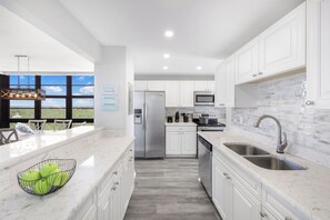 Een moderne keuken met witte kasten, roestvrijstalen apparatuur en een groot raam met uitzicht op een mooi landschap.