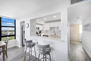 A modern kitchen with white cabinets, a central island, and a view of the city.