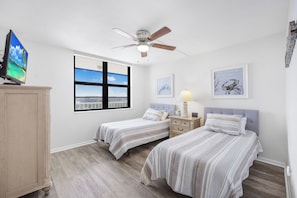 A bedroom with two beds, a ceiling fan, a window with a view, and artwork on the walls.