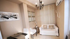 A living room with a white sofa, a small table with a glass bowl, a chair, a chandelier, and a wall-mounted air conditioner. - Apartamento Constitución Málaga (Málaga)