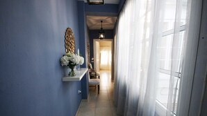 A hallway with a blue wall, a white shelf with a vase of flowers, and a door with sheer curtains. - Apartamento Constitución Málaga (Málaga)