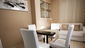 A dining area with a table and four white chairs, a sofa with patterned cushions, and a wall-mounted painting. - Apartamento Constitución Málaga (Málaga)