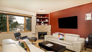 Una sala de estar con chimenea, un ventanal amplio, un televisor de pantalla plana y un sofá.