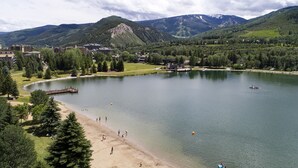 Un resort junto al lago con una playa de arena, un muelle y vistas a montañas al fondo.