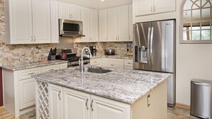 Una cocina moderna con armarios blancos, encimeras de granito, electrodomésticos de acero inoxidable y un microondas integrado.