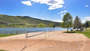 Cancha de voleibol de playa con red, arena y vista al lago.
