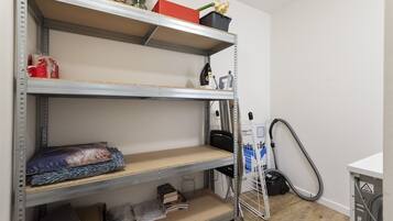 Uno spazio di stoccaggio con scaffali metallici, un aspirapolvere e una scala.