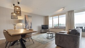 A modern living room with a dining table, sofa, TV, and large windows. - Spacious and luxurious apartment - Kaag Resort (27) (Warmond)