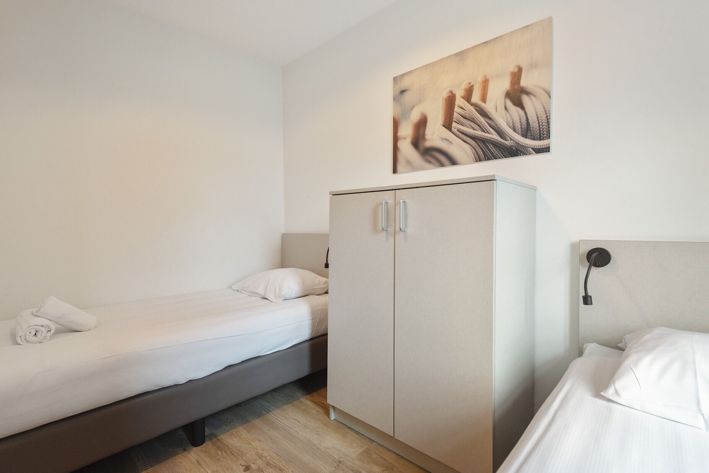 Una habitación pequeña y limpia con una cama, un armario y un cuadro en la pared.