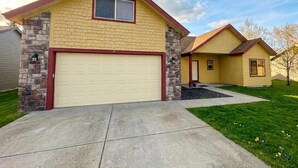 A two-story house with a garage, stone foundation, and a well-maintained lawn.