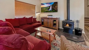 A cozy living room with a red sofa, a wooden coffee table, a TV, a fireplace, and a painting of a waterfall.