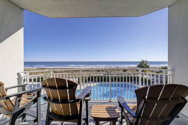 A balcony with a pool, chairs, and a view of the ocean.