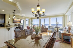 A spacious living area with a large glass table, wicker furniture, and a view of the ocean.