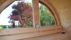 Een houten hut met een groot rondboogvenster met uitzicht op een boom met rode bladeren.
