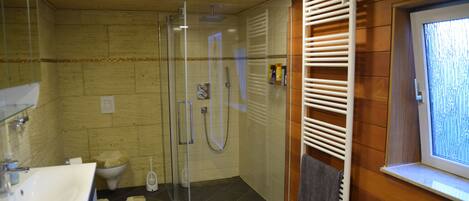 A bathroom with a glass shower enclosure, a white sink, and a towel rack.