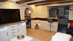 Een moderne woonkamer met een flatscreen televisie, witte kasten, een accentmuur van steen en een gezellige zithoek.