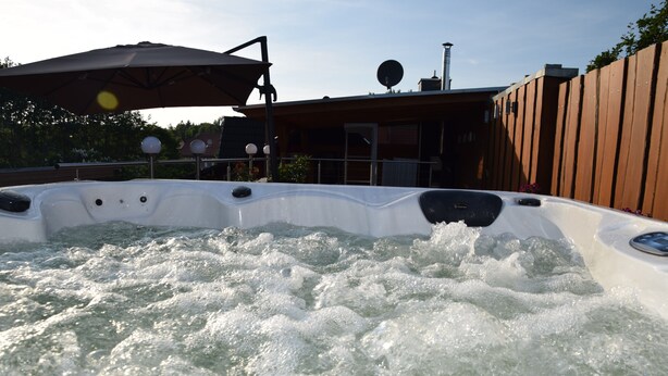 Een hottub met waterstralen, een parasol en een gebouw op de achtergrond.