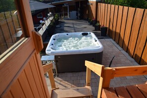 Un bain à remous installé sur une terrasse en bois, avec une maison visible au loin.