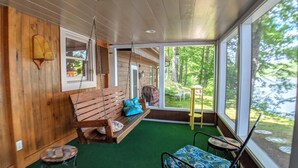 Ein Holzblockhaus-Interieur mit Schaukelstuhl, einem kleinen Tisch und Blick ins Freie.