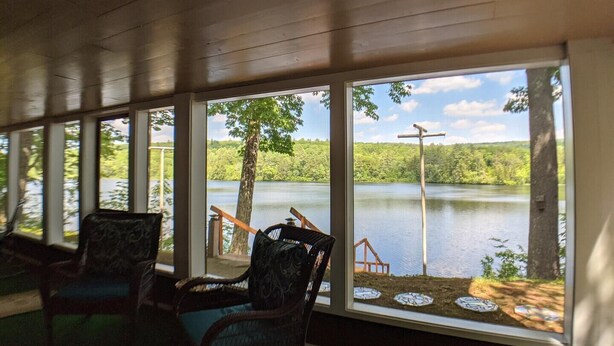 Ein Zimmer mit großen Fenstern und Blick auf einen See, einer Holzbalkendecke und zwei Fenstertische.