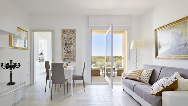 A modern living room with a sofa, a dining table with chairs, a chandelier, and a view of the outdoors. - Sea view five minutes from the beach IUN Q5161 (Quartu Sant'Elena)