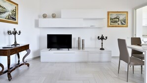 A modern living room with a flat-screen TV, white cabinetry, a dining table with chairs, and artwork on the walls. - Sea view five minutes from the beach IUN Q5161 (Quartu Sant'Elena)