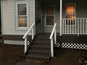 A house with a front porch, a set of wooden stairs, and a white picket fence.