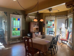 A dining area with a long table, chairs, pendant lights, and a view through the windows. - A Bonnie Place 3.2 miles from All Star Village (Oneonta)