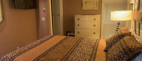 A bedroom with a bed, a dresser, a television, and a lamp.