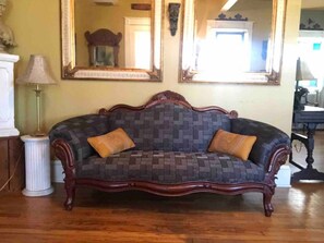Un canapé de style vintage, recouvert d’un tissu à motifs et agrémenté de deux coussins, est placé dans une pièce dotée d’un plancher en bois et d’un grand miroir mural.