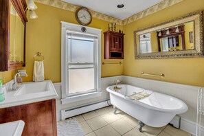 Une salle de bain avec une baignoire sur pieds, un lavabo, un miroir et une fenêtre.