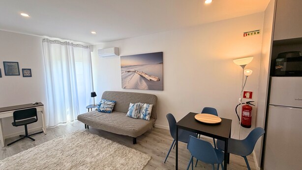 En moderne stue med sofa, spisebord med stole, fladskærms-tv og køleskab.