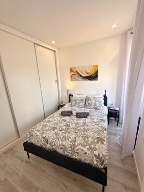 Quarto com cama, mesa de cabeceira, uma obra de arte na parede e porta.